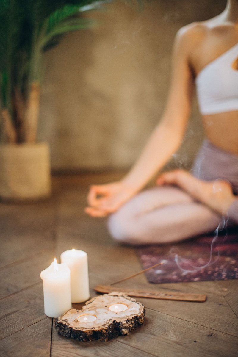 Woman meditating cross-legged on a mat beside lit candles and incense on a wooden floor