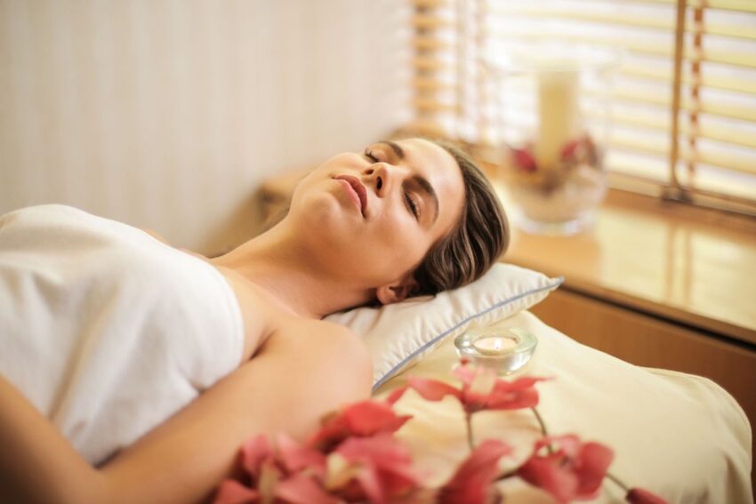 Woman resting with her eyes closed on a treatment bed, with a small candle and pink flowers nearby